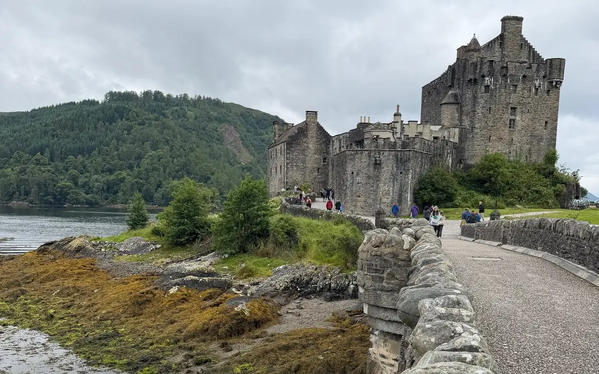 A stone parapet along the path to Eilean Donan Castle, with visitors walking towards the gate