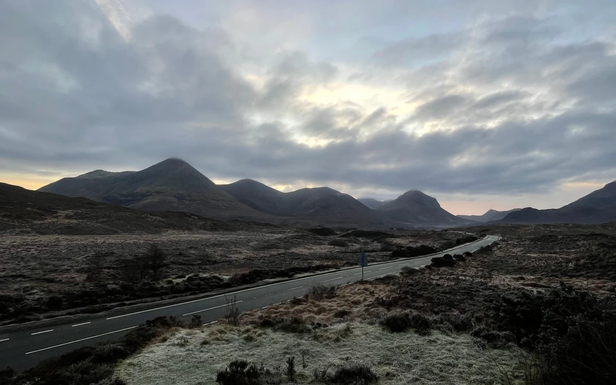 Una carretera que cruza un páramo escarchado hacia una línea de cumbres bajo nubes densas