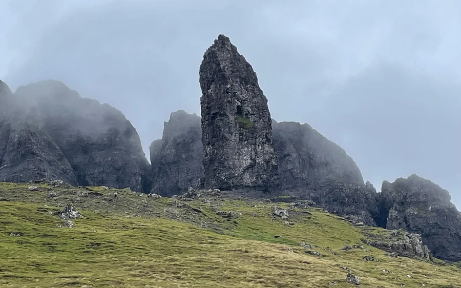 Una guglia rocciosa scura tra cime nebbiose sopra un pendio erboso