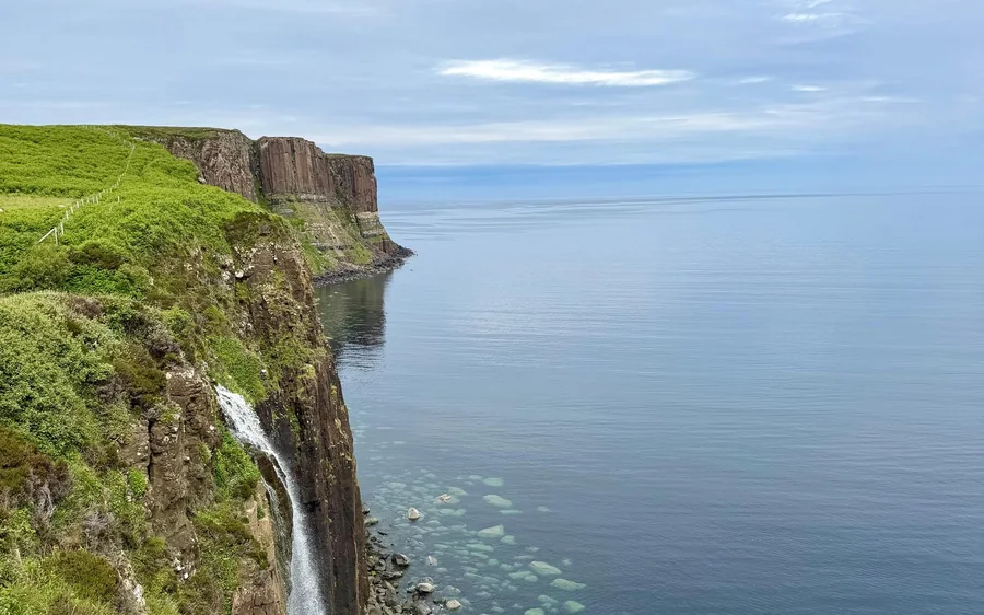 Una cascata che precipita da scogliere marine verdi in un mare calmo