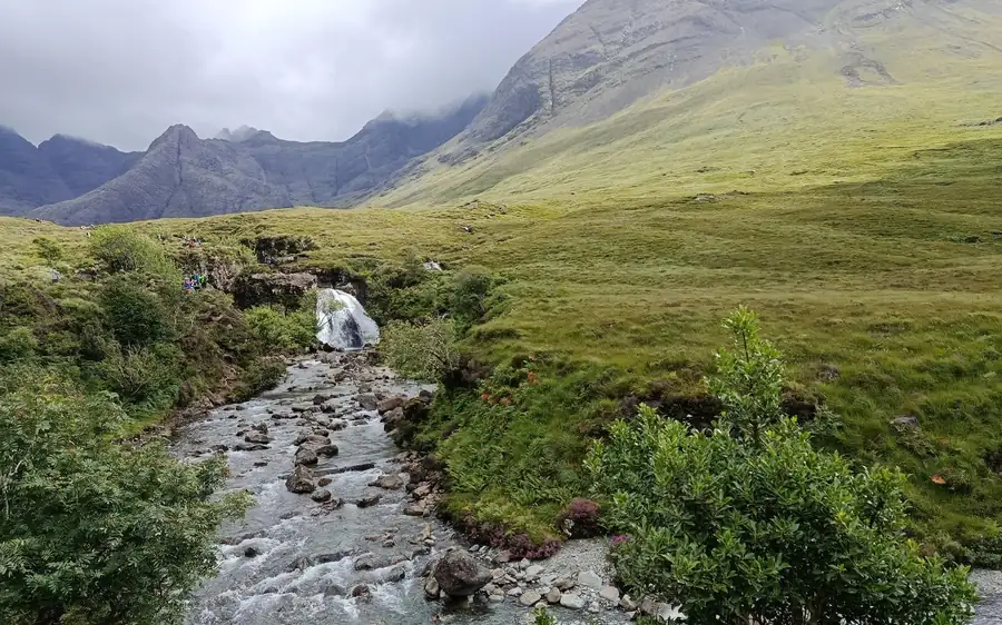 Un ruscello roccioso e una piccola cascata in una valle verde sotto cime nebbiose