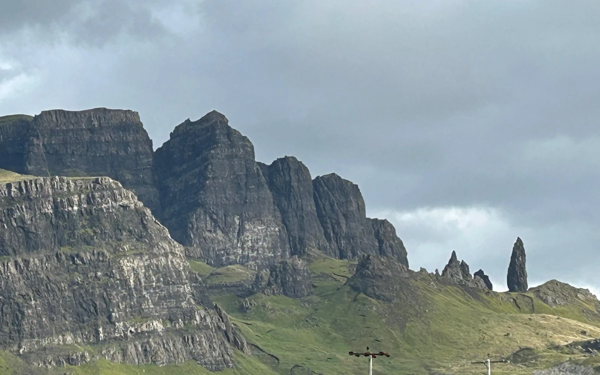 Grey layered cliffs with a lone rock pinnacle standing to the right, above green slopes