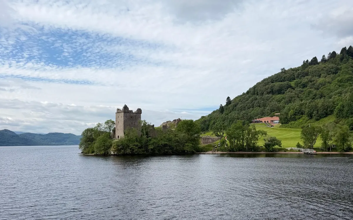 A ruined castle tower on a wooded point, with wide water in front and a forested hill behind
